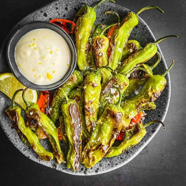 shishito peppers with dipping sauce on a plate.