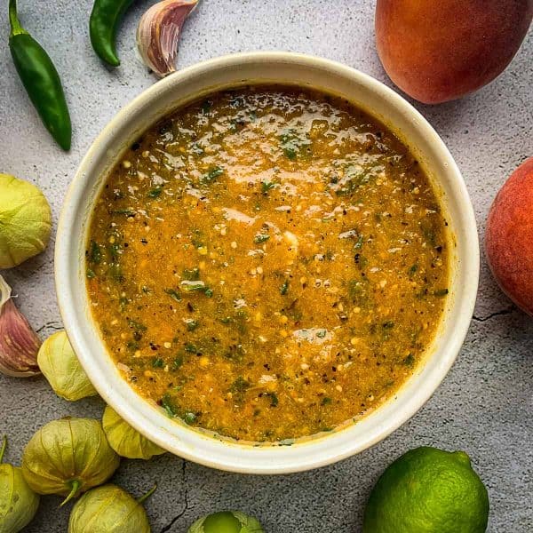 Peach tomatillo salsa in a bowl surrounded by ingredients.