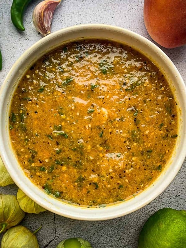 Peach tomatillo salsa in a bowl surrounded by ingredients.