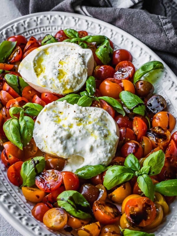 Platter of sliced cherry tomatoes and burrata cheese with basil.