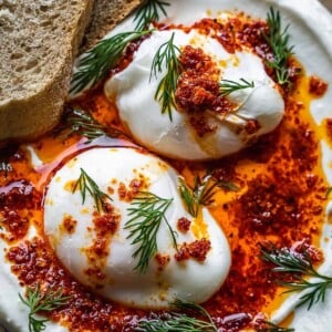 Poached Turkish eggs with dill and chili oil on a plate.