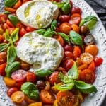 Sliced cherry tomatoes, with basil leaves and an open ball of burrata cheese.