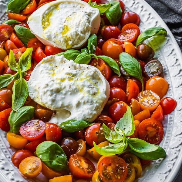 Sliced cherry tomatoes, with basil leaves and an open ball of burrata cheese.