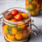 Cherry tomatoes with dill and garlic in a pickling jar.