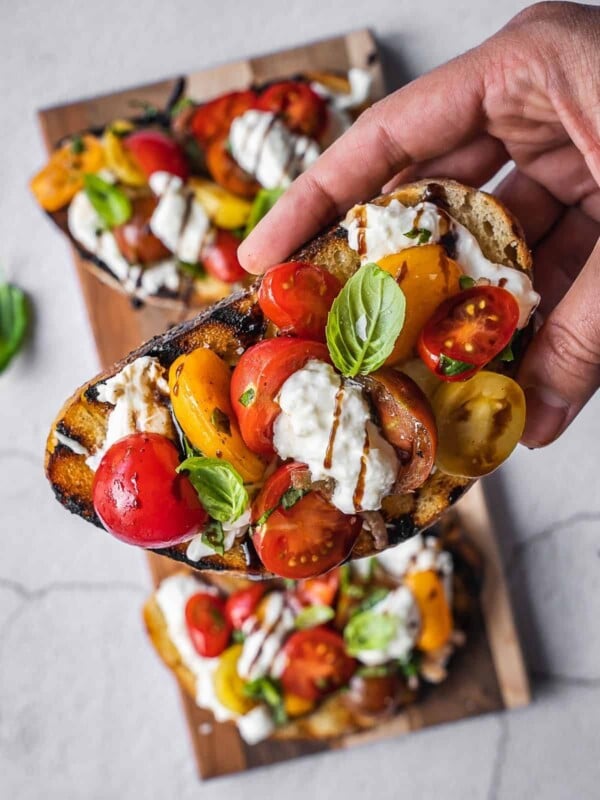 A hand holding a burrata bruschetta with tomatoes and basil.