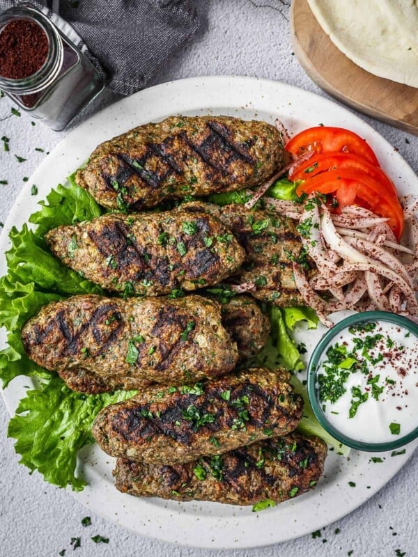 chicken kafta pieces on a plate with yogurt sauce, tomatoes and onions.