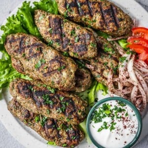 chicken kafta pieces on a plate with yogurt sauce, tomatoes and onions.