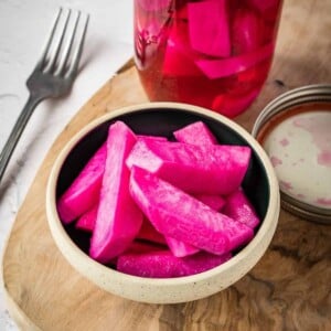 Pink pickled turnips in a bowl on a board.