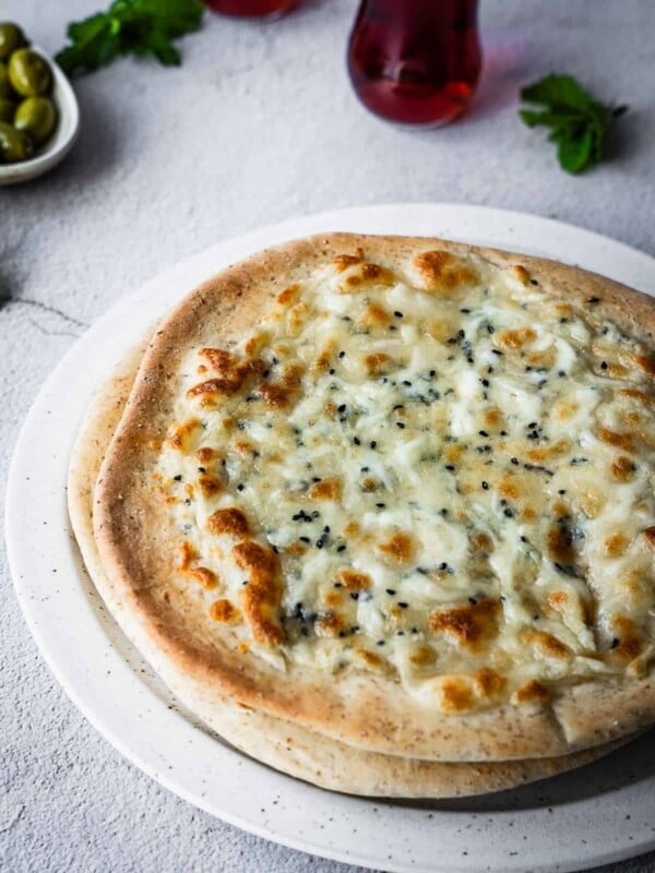 Cheesy flatbreads on a plate with olives and mint tea on the side.