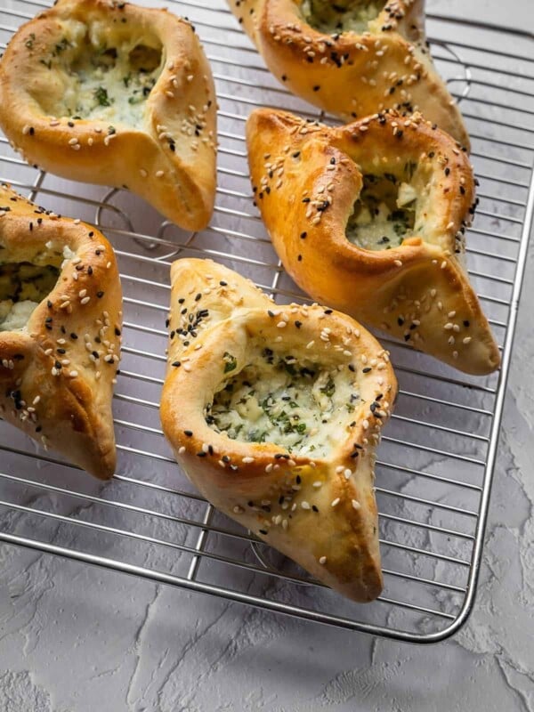 Cheese and herb fatayer pastries with sesame seeds on a cooling rack.