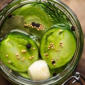 Overhead shot of a jar of pickled sliced green tomatoes and spices on a wooden board.