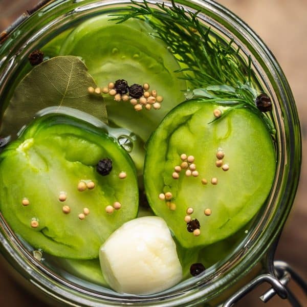 Overhead shot of a jar of pickled sliced green tomatoes and spices on a wooden board.