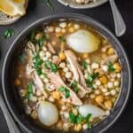Bowl of chicken, chickpea and couscous on a marble table with a side lemon and extra couscous.