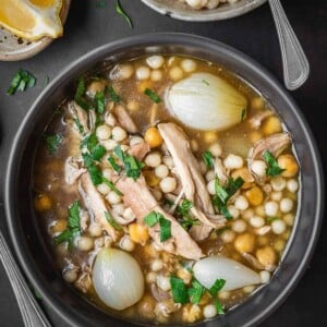 Bowl of chicken, chickpea and couscous on a marble table with a side lemon and extra couscous.