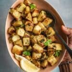 Bowl of spicy and herby potatoes with lemon wedges on the side.