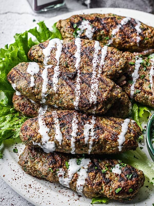 Beef kofta on a plate with a side of vegetables and drizzled with yogurt sauce.