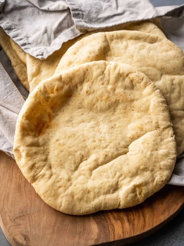 A stack of pitas nestled in a towel on a wooden board.