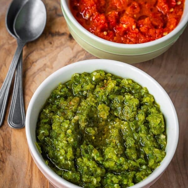 Two bowls of chili paste, one green and one red, on a wooden board.