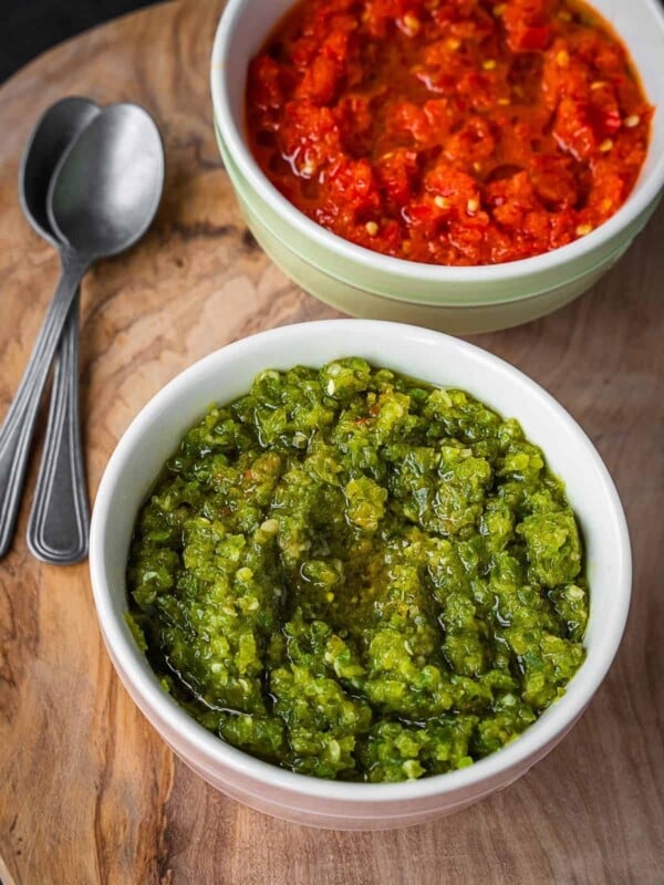 Two bowls of chili paste, one green and one red, on a wooden board.