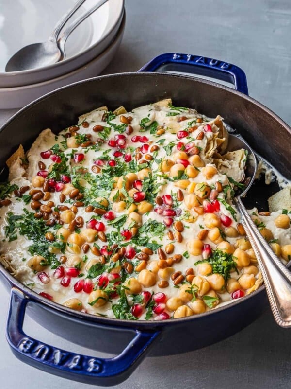 A casserole dish with creamy fattet hummus, garnished with fresh parsley, pine nuts and pomegranate seeds.