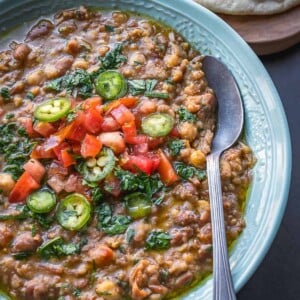 Bowl of mashed fava and chickpeas topped with diced tomatoes and parsley.