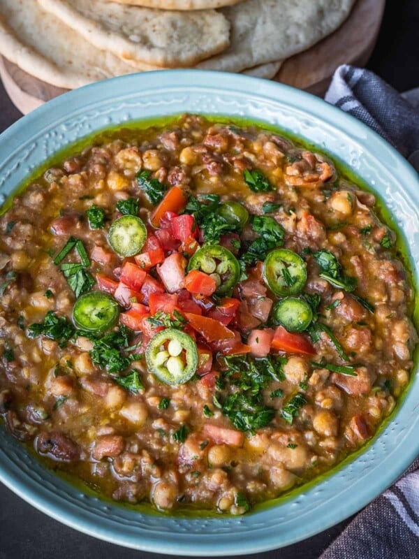 Bowl of mashed fava and chickpeas topped with diced tomatoes and parsley.