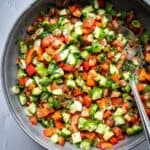 Bowl of chopped cucumbers, tomatoes, peppers and herbs.