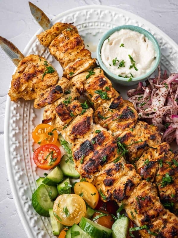 A plate of shish tawook skewers with a side salad, pickled sumac onions and garlic sauce.