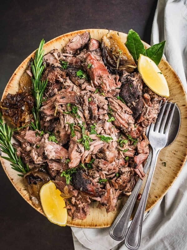 A plate with pulled lamb and herb garnish.