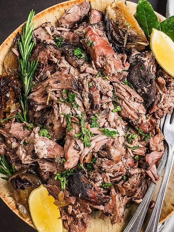 A plate with pulled lamb and herb garnish.