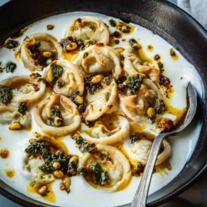 Bowl of shish barak garnished with pine nuts and parsley.