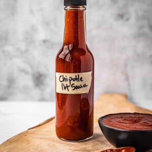 Bottle of hot sauce on a board next to a small bowl with the same hot sauce.
