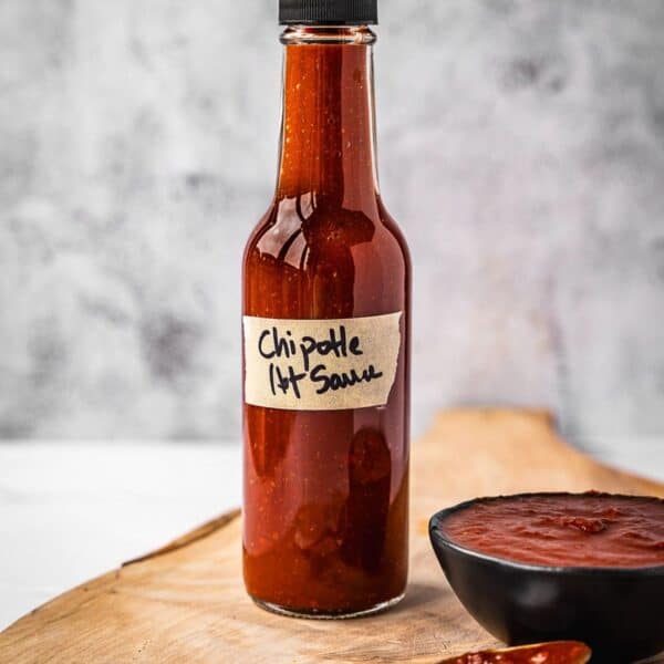 Bottle of hot sauce on a board next to a small bowl with the same hot sauce.