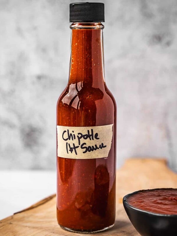 Bottle of hot sauce on a board next to a small bowl with the same hot sauce.