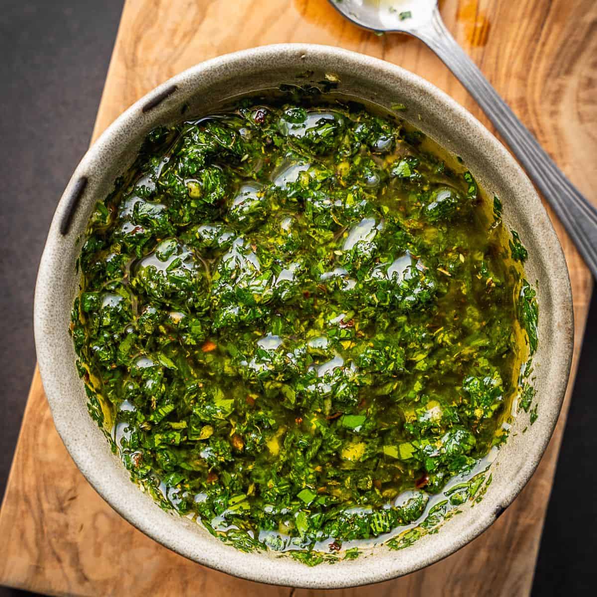 Bowl of green salsa on a wooden cutting board.