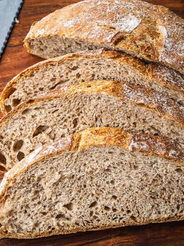 Sliced no knead whole wheat bread on a wooden cutting board.