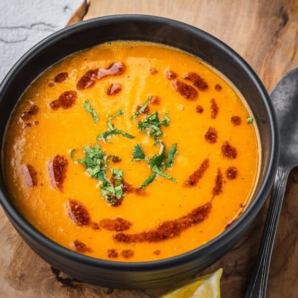 Bowl of mercimek corbasi red lentil soup garnished with chili oil and cilantro.