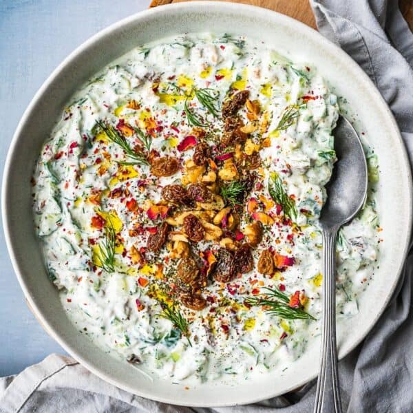 Bowl of mast-o khiar dip, garnished with rose petals, nuts, raisins and herbs.