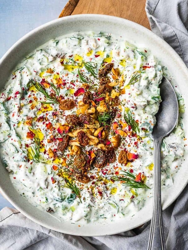 Bowl of mast-o khiar dip, garnished with rose petals, nuts, raisins and herbs.