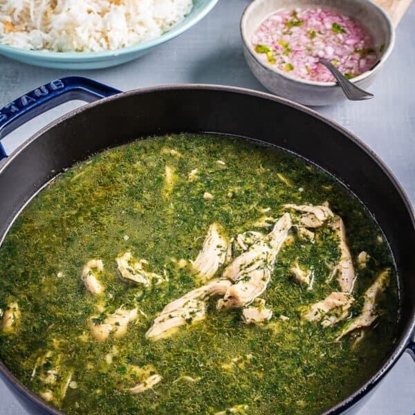 A pot of molokhia stew with a side of rice, chopped onions and lemons.