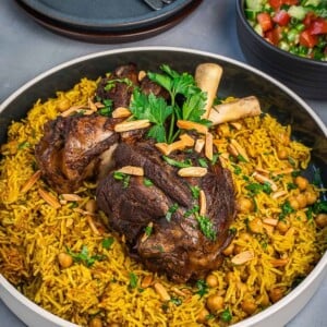 A large bowl of rice and chickpeas topped with tender lamb shanks with a side of chopped salad.