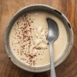 Creamy tahini sauce garnished with sumac in a bowl with a spoon.