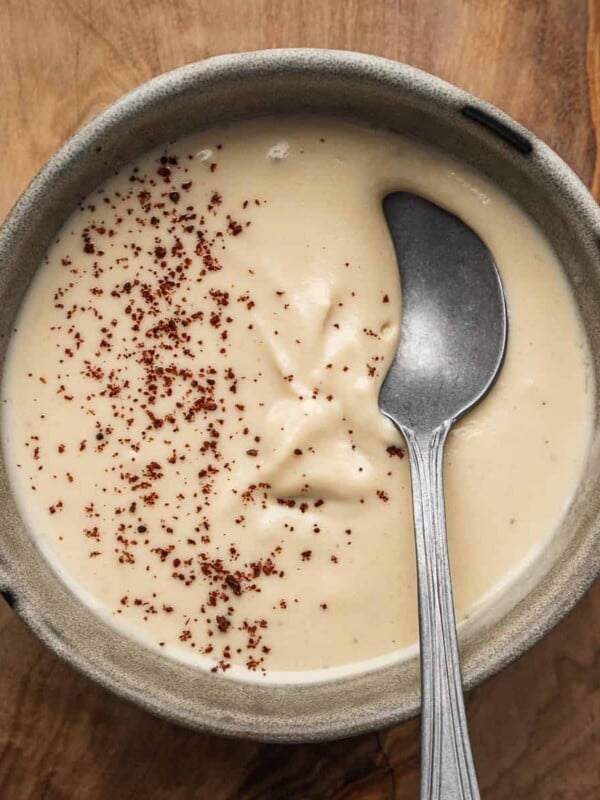 Creamy tahini sauce garnished with sumac in a bowl with a spoon.