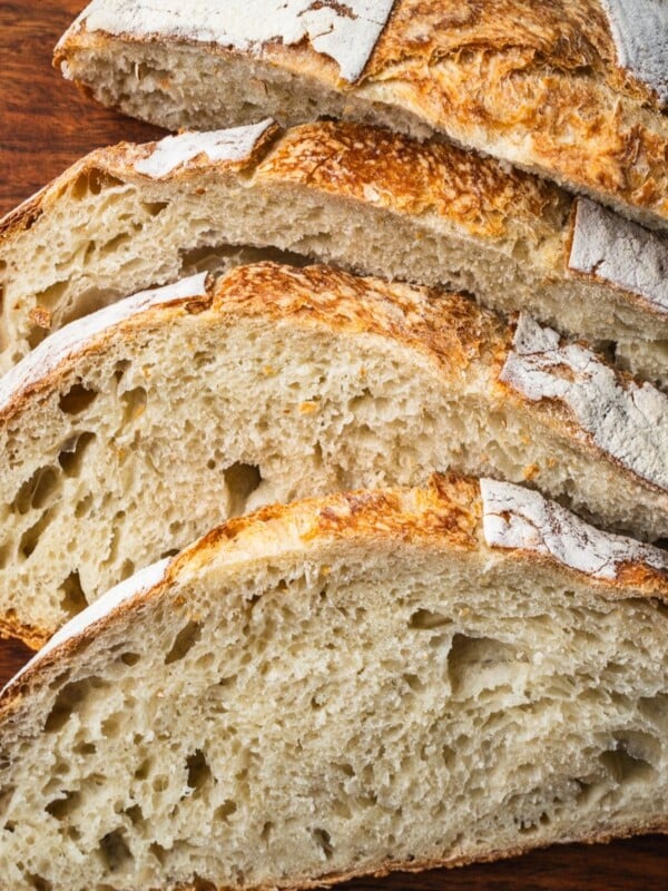 A loaf of no knead white bread sliced on a wooden board.