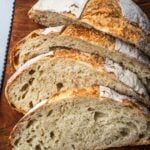 A loaf of no knead white bread sliced on a wooden board.