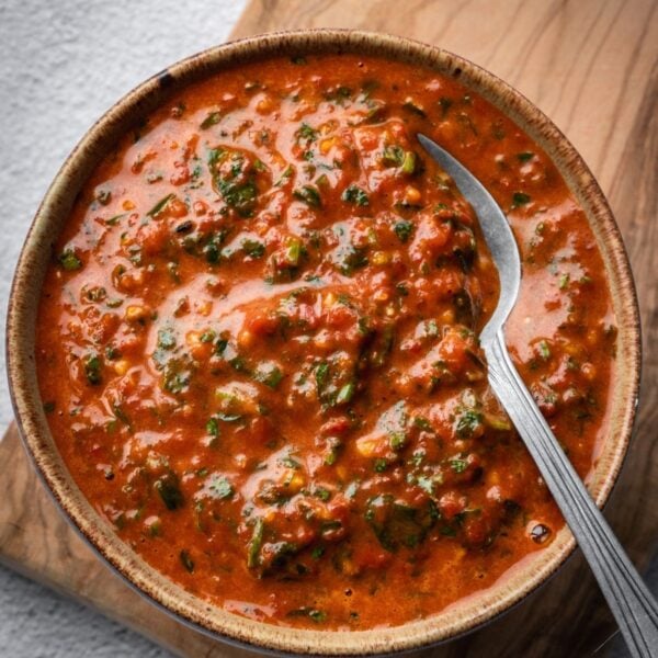 Red chimichurri in a small bowl set on a wooden board.