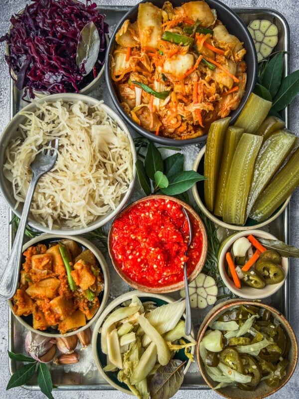 A tray with several different types of fermented foods such as sauerkraut, dill pickles, radishes, jalapenos and more.