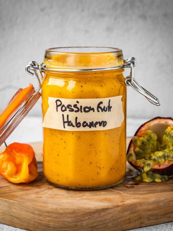 Passion fruit habanero in a jar with a fresh habanero pepper and an opened passion fruit on a board.