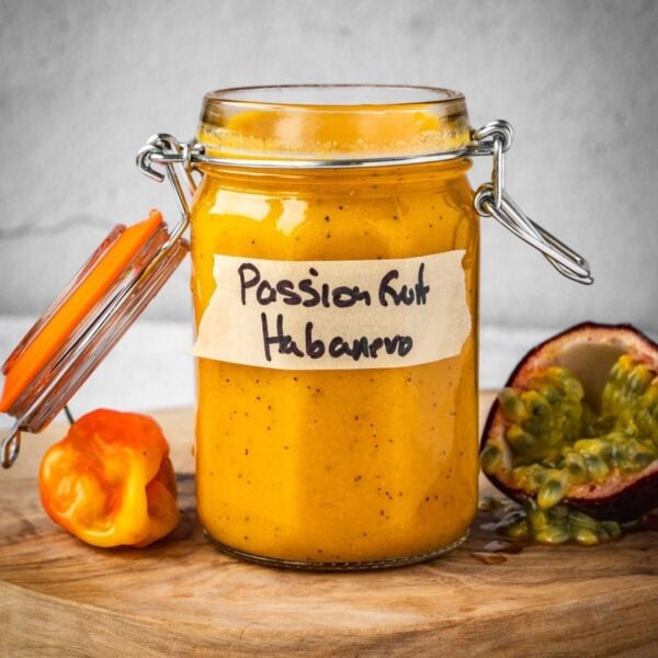 Passion fruit habanero in a jar with a fresh habanero pepper and an opened passion fruit on a board.
