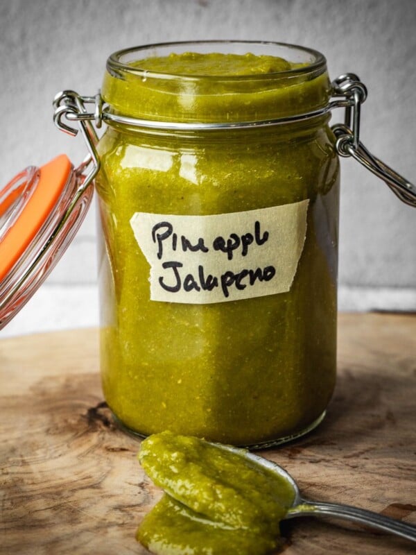 A jar of pineapple jalapeno hot sauce on a wooden board.